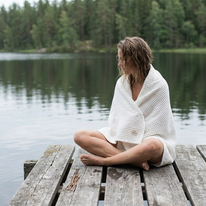 Kvinna med vit våffelhandduk i linne på brygga vid insjö – Noémie Living