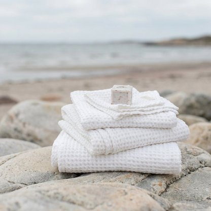 Vikta vita våffelhanddukar i linne på strand – Noémie Living